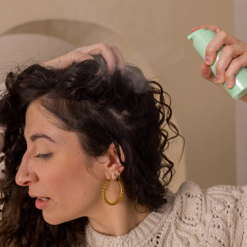 Vrouw gebruikt Curl Bites - Volumizing Dryshampoo - 20gr op krullend haar voor extra volume en een frisse hoofdhuid zonder wassen.