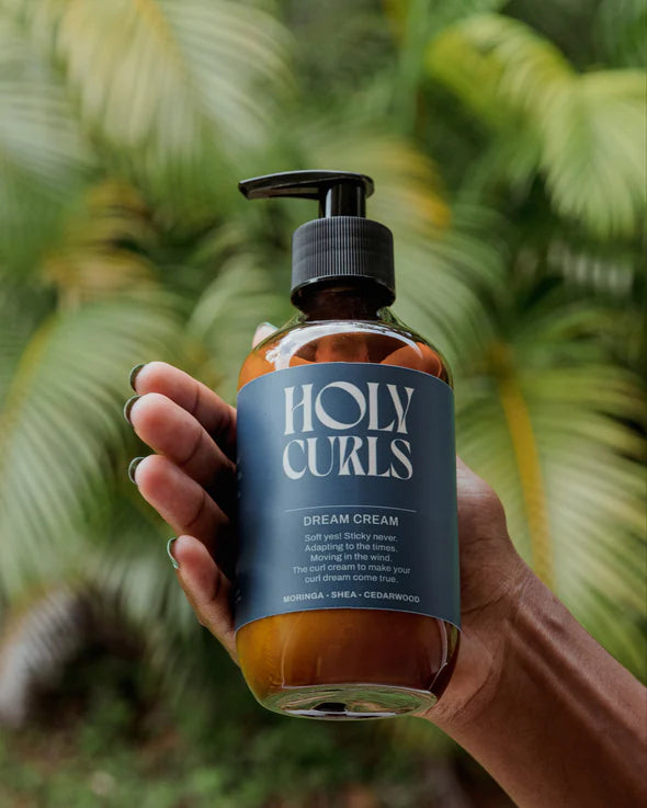 Holy Curls, Curl Cream | 300 ml vastgehouden in hand met tropische achtergrond, perfect voor verzorging van natuurlijke krullen.