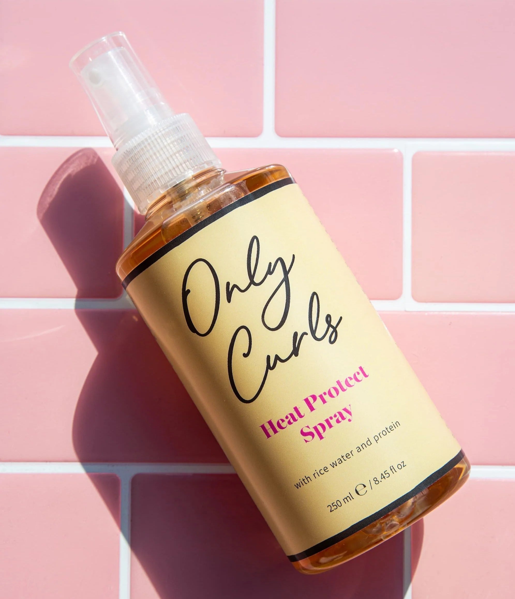 Only Curls Heat Protect Spray haarspray op roze tegelachtergrond, beschermt krullend haar tegen hitte, vervuiling en UV-straling.