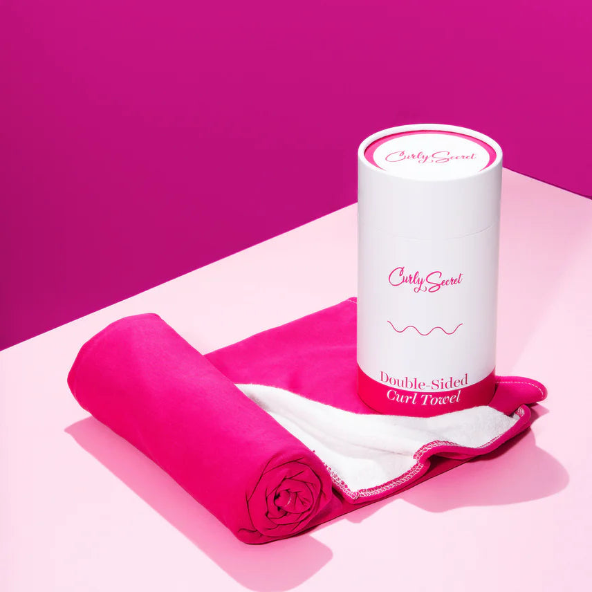 Curly Secret Dubbelzijdige Krul handdoek in fuchsia met witte binnenzijde, gepresenteerd naast luxe verpakking op roze achtergrond.