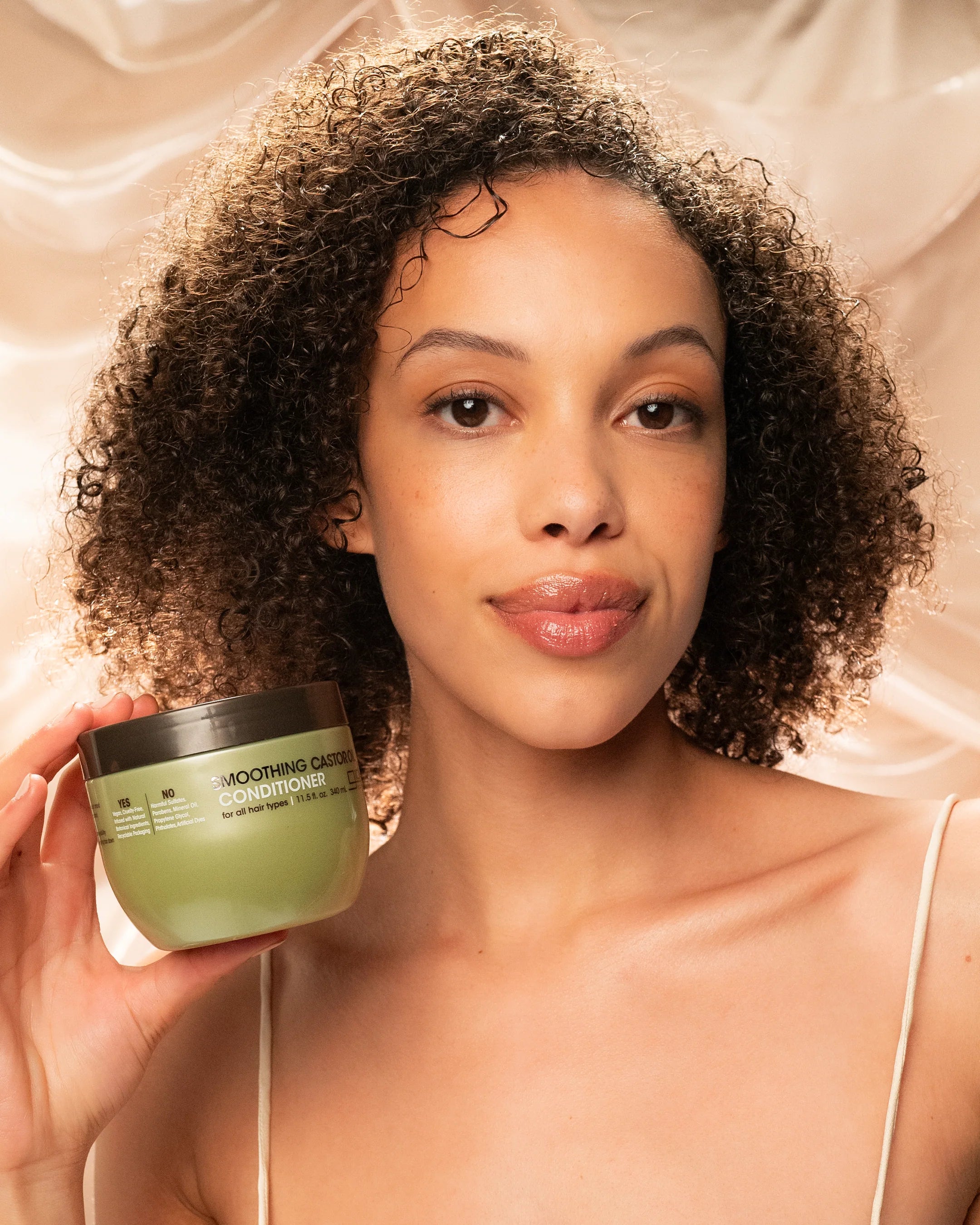 Model met krullend haar toont Giovanni Cosmetics Castor Oil leave-in conditioner -340ml, ideaal voor CG-haarverzorging en dagelijkse hydratatie.