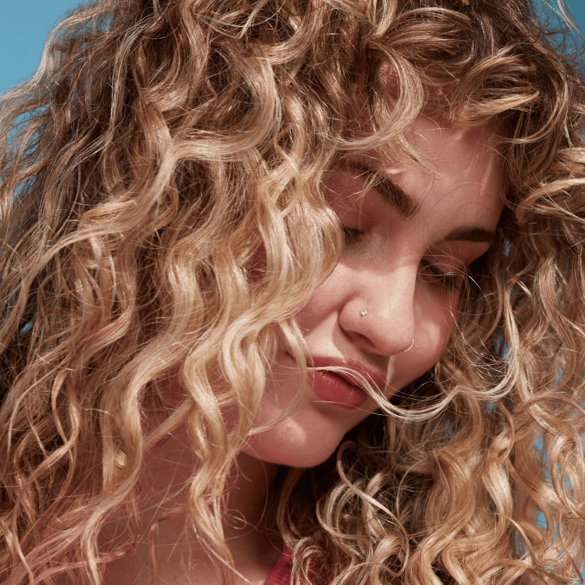 Model met gedefinieerde krullen gestyled met Umberto Giannini Curl Foam, toont natuurlijk volume en beach waves effect.