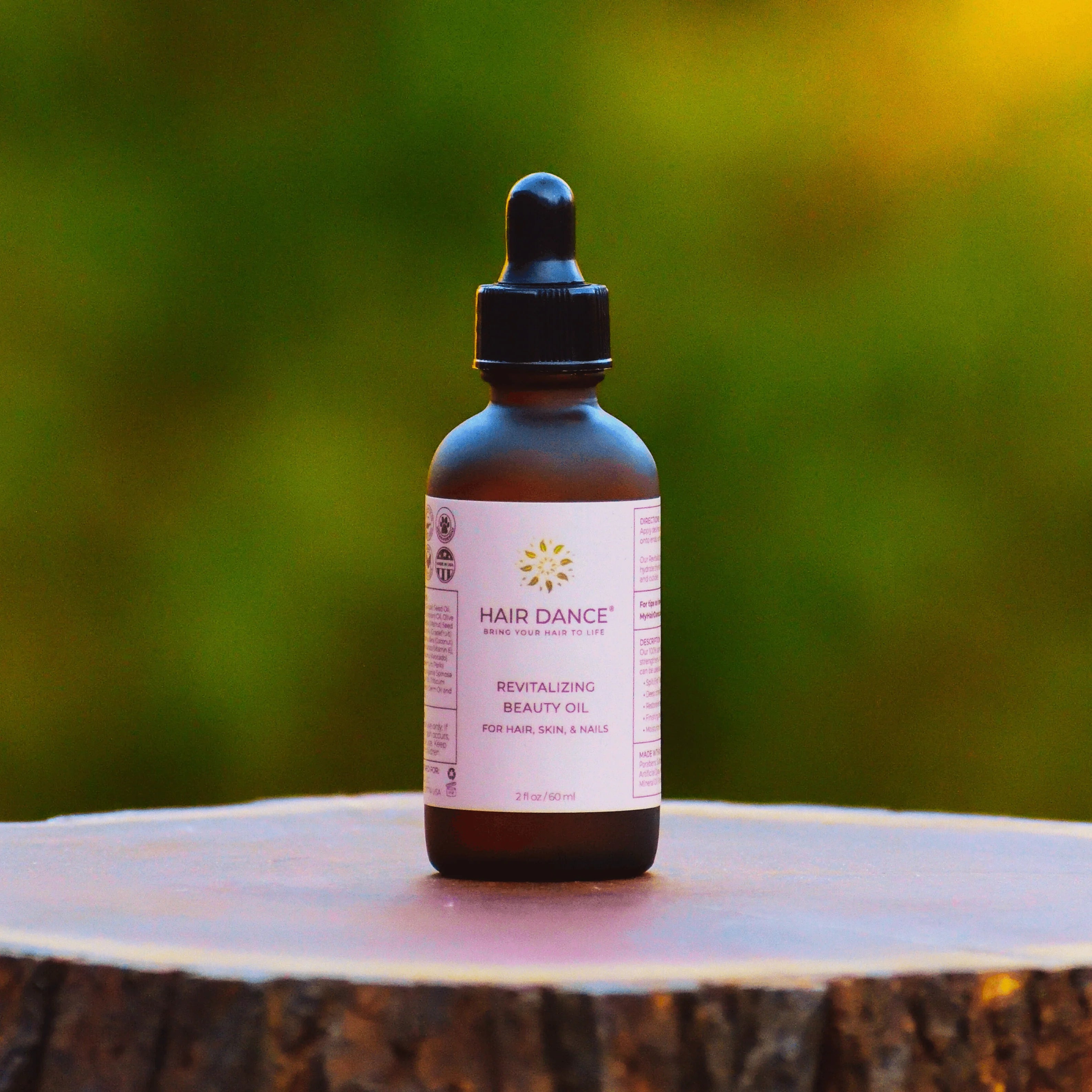 Hair Dance Revitalizing Beauty Oil 60 ml op een boomstronk met natuurlijke achtergrond, ideaal voor haar-, huid- en nagelverzorging.