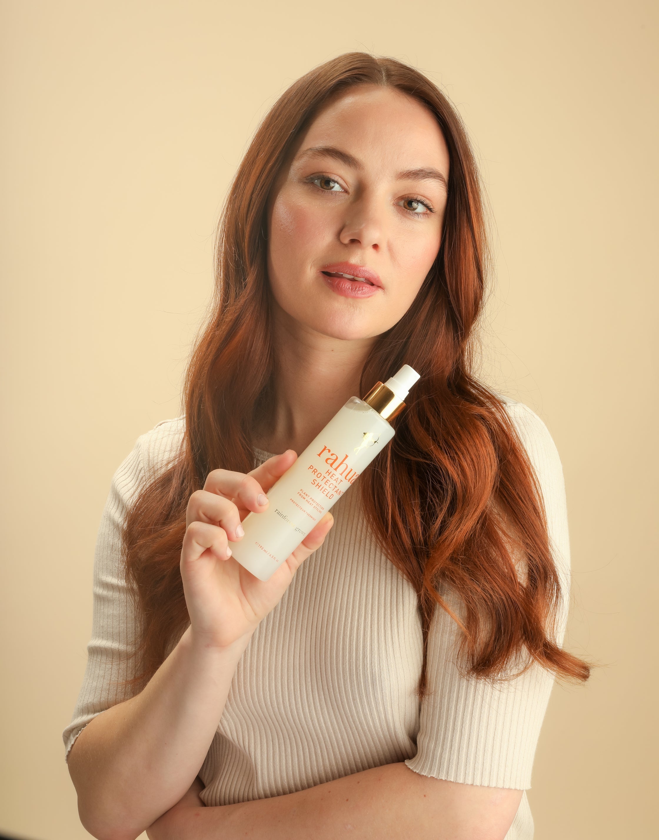 Vrouw met lang roodbruin haar toont Heat Protectant Shield - Rahua - 193ml, een vegan haarolie voor bescherming tegen hittetools en styling.