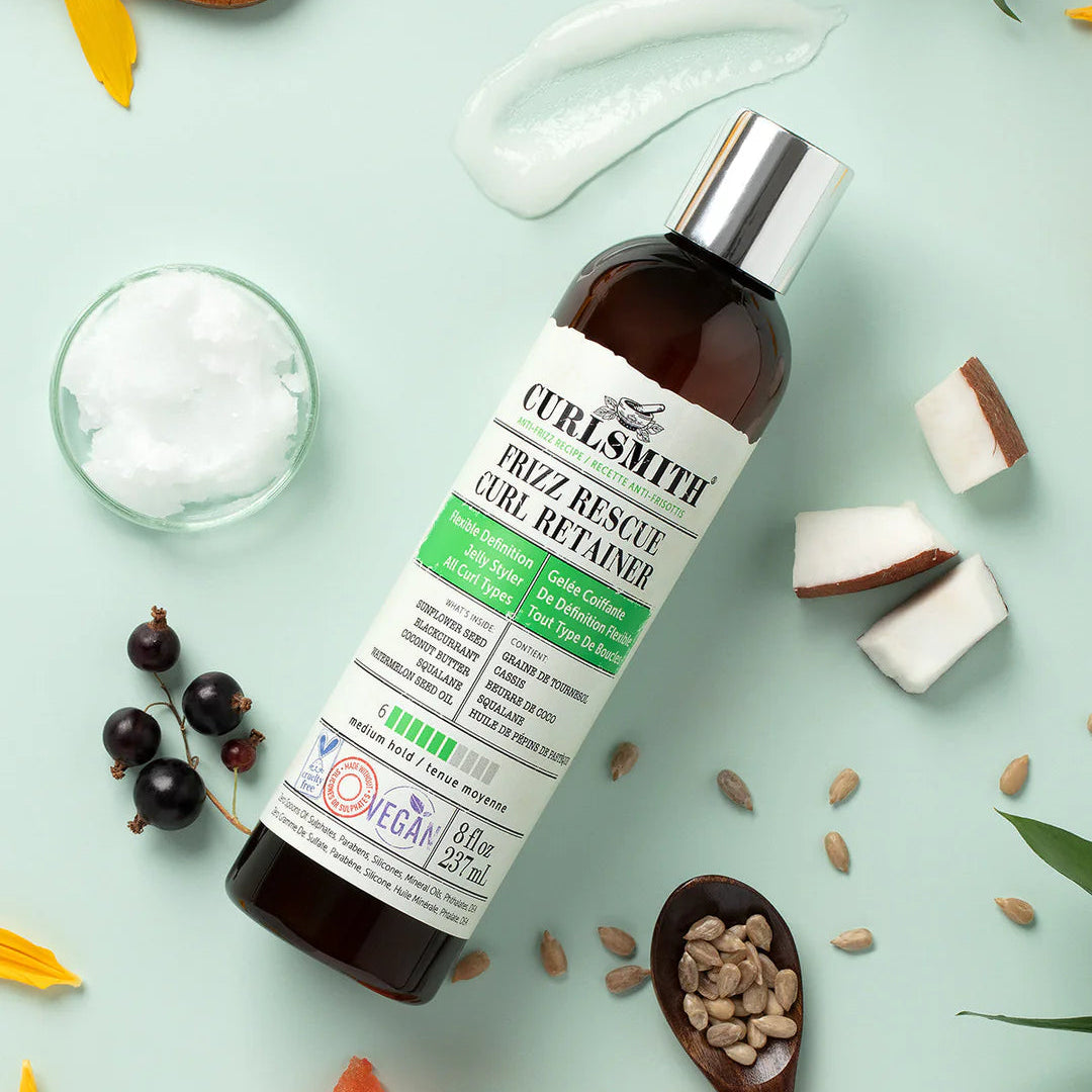 Curlsmith Frizz Rescue Curl Retainer omringd door natuurlijke ingrediënten zoals kokos, zonnebloempitten en zwarte bessen voor gezonde krullen.
