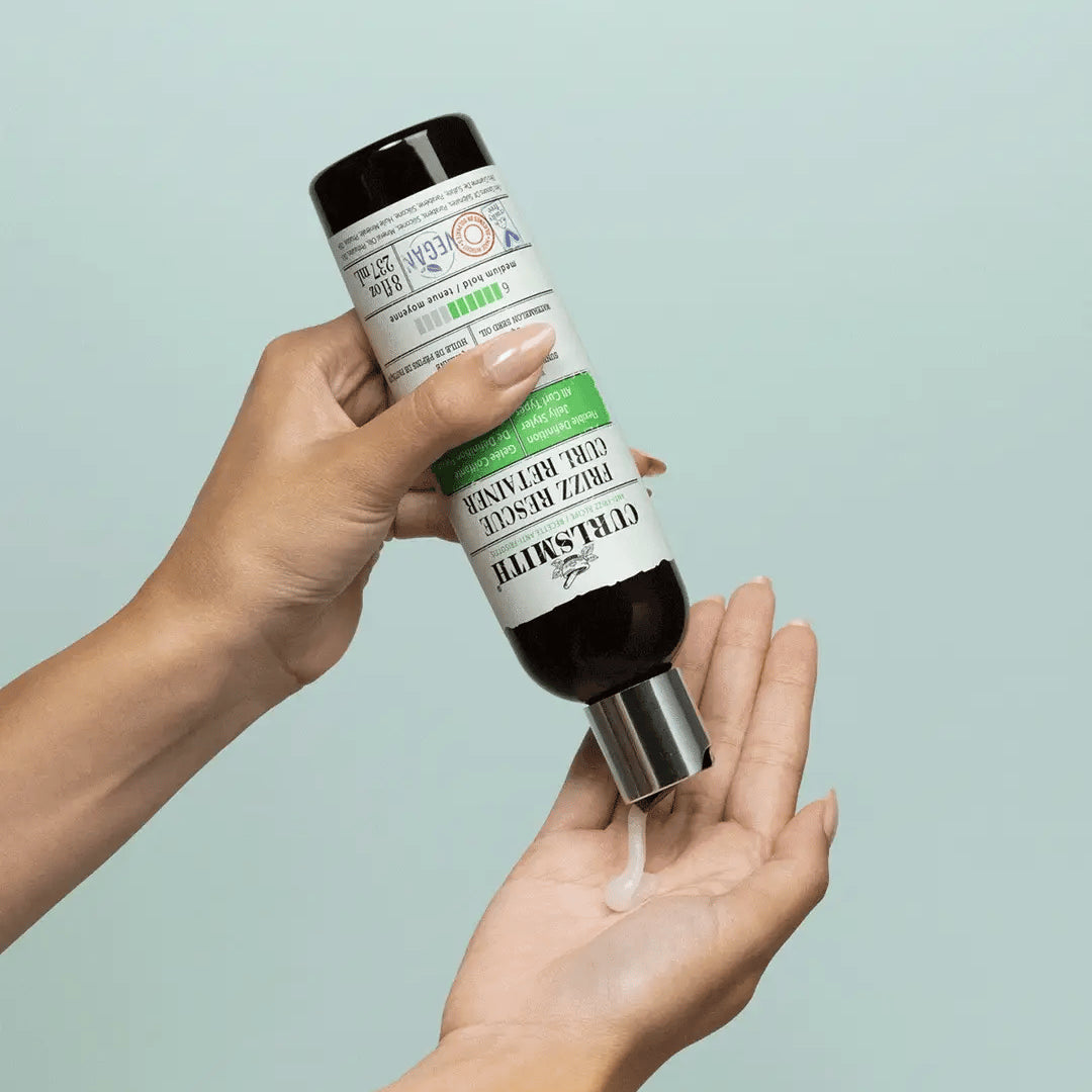 Hand die Curlsmith Frizz Rescue Curl Retainer styling gel aanbrengt, toont de textuur van het product voor kruldefinitie zonder pluis.